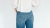 Woman from behind wearing a white blouse and blue jeans against a plain white background.
