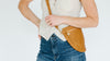 A person in blue jeans holds two reusable mesh bags, one containing oranges, standing against a white background.