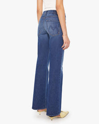 A woman, seen from the back, wears Mother’s The Bookie Sneak in Perfectly Imperfect—high-rise bootcut jeans in semi-rigid denim—with a white sleeveless top and cream pointed-toe shoes.