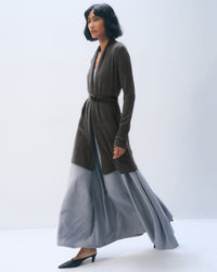 A woman with a short bob wears a White & Warren Cashmere Trapeze Cardigan in Dark Slate Heather over a flowing light gray skirt and black heels, walking against a plain, light background.