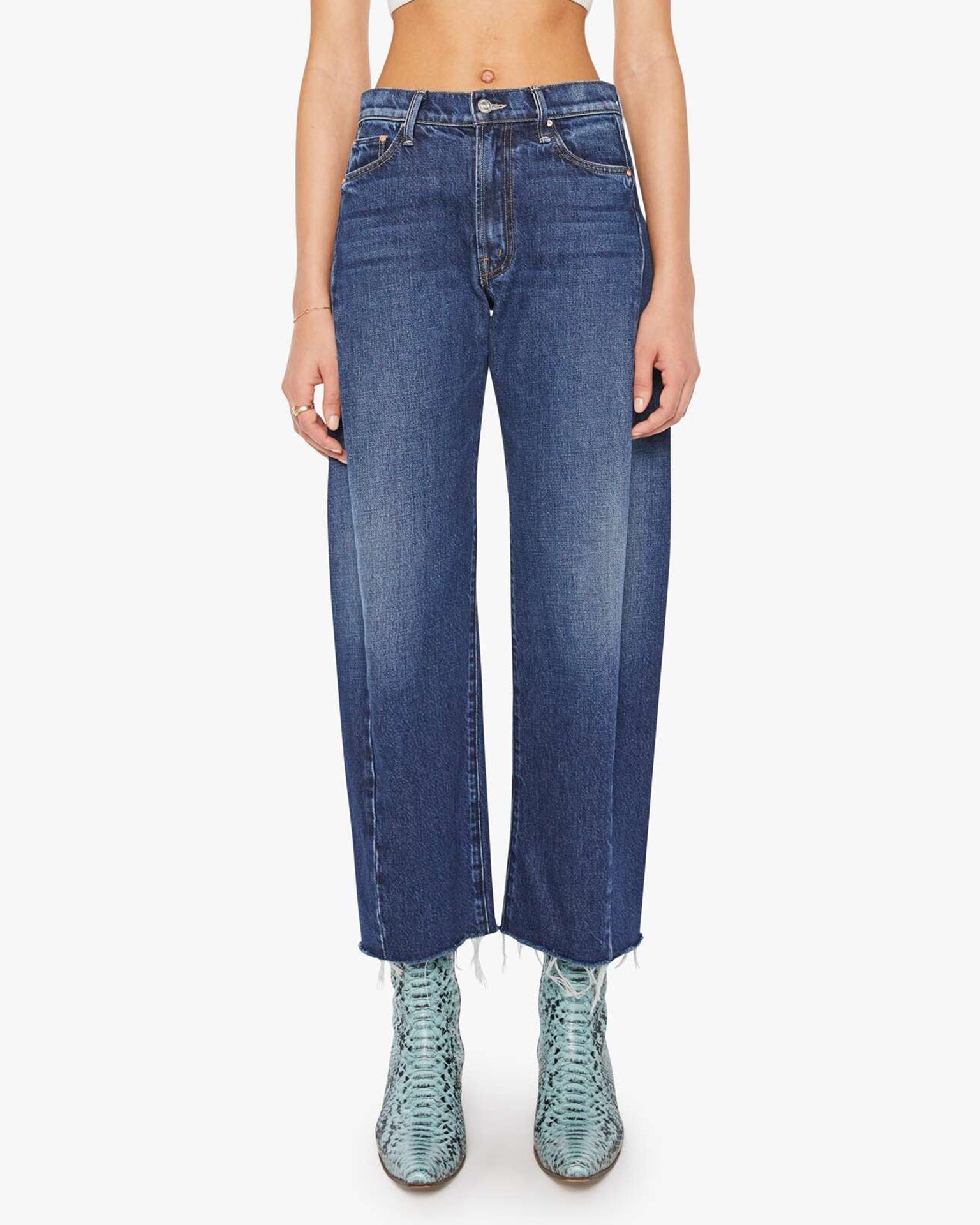 A person wears MOTHER's Mid Rise Full-Pipe Flood Fray jeans in Unplugged with a raw hem, front fading, and classic five-pocket styling, paired with textured light blue boots. The upper body is not fully visible.