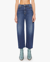 A person wears MOTHER's Mid Rise Full-Pipe Flood Fray jeans in Unplugged with a raw hem, front fading, and classic five-pocket styling, paired with textured light blue boots. The upper body is not fully visible.