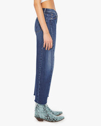 A person stands in profile wearing Mother’s Mid Rise Full-Pipe Flood Fray in Unplugged jeans and light blue snakeskin-print ankle boots against a plain white background.