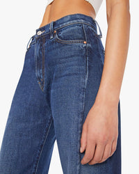 A person wears Mother’s Mid Rise Full-Pipe Flood Fray in Unplugged dark blue denim and a white ribbed crop top. The image focuses on the waist and hips, showcasing the jeans’ button and pocket details.