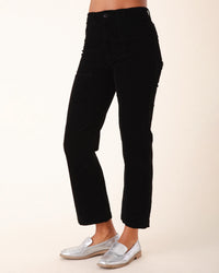 A person stands against a plain light background, showing only their lower torso and legs, wearing Prairie Underground's Corduroy Carpenter Pant in Black with silver loafers.