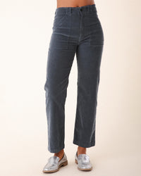 A person wears Prairie Underground's Corduroy Carpenter Pant in Cruiseliner blue with silver loafers, standing against a plain light background. Only the lower torso and legs are visible.