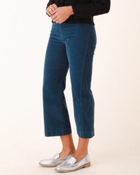 A person showcases Prairie Underground’s Knack Cords in Atlantic—stylish fitted corduroy flared pants—paired with a black top and silver loafers, standing against a plain light background. The photo is cropped at the shoulders.