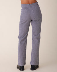 A person wearing Prairie Underground's Long Smithy Pant in Oyster with thin blue and white stripes, viewed from the back, paired with black shoes against a neutral background.
