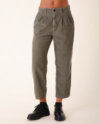 A person wears Prairie Underground's Double Pleat Cords in Eucalyptus with black lace-up shoes. Only their body from waist to ankles is shown against a light background.