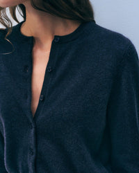 A woman wears a White & Warren Cashmere Crewneck Cardigan in Deep Navy, partially unbuttoned, shown from shoulders to mid-torso against a light background.