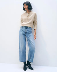 A woman with a short bob wears the White & Warren Cashmere Luxe Henley in Natural Heather, light blue wide-leg jeans, and black ankle boots, standing against a plain white background.