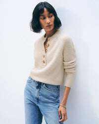 A woman with short dark hair wears the White & Warren Cashmere Luxe Henley in Natural Heather and light blue jeans, standing against a plain white background and looking to the side with a relaxed expression.