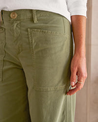 A person stands indoors wearing Frank & Eileen’s Limerick Wrap Pocket Pant in Olive and a white long-sleeve shirt, with their right hand by their side and the pant’s large pocket visible.
