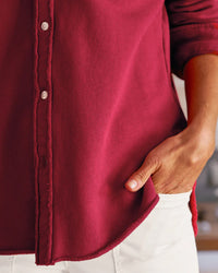 Wearing a Frank & Eileen Eileen-Relaxed Button Up Shirt in Garnet French Terry with white pants, a person stands with one hand in their pocket. The photo is cropped to show only the torso and hand.