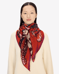 A woman with straight black hair wears a cream ribbed sweater and the Inoui Editions Square / Carre 130 Papillons in Red scarf around her neck, set against a plain light background.