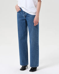 A person wearing a white T-shirt, black heeled shoes, and AGOLDE's Low Rise Loose in Charge jeans stands with one hand in their pocket against a plain light background.