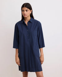 A woman wearing the Hartford Rank Henley Dress in Midnight—a casual, navy knee-length cotton poplin shirtdress with a button-up front and three-quarter sleeves—stands against a plain light background.