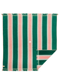 The Business & Pleasure Co Beach Blanket - Bistro Green Stripe is a family-friendly 100% cotton rectangular blanket with green and pink stripes, fringed edges, a small central hole, and a folded corner showing the underside.