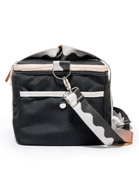 The Premium Cooler Bag - Rivie Black by Business & Pleasure Co is a black, rectangular, eco-friendly bag with a white zippered front pocket and a detachable striped shoulder strap for a vintage-inspired look.