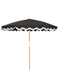 The Amalfi Umbrella - Rivie Black by Business & Pleasure Co features a black UV water-resistant canopy with white scalloped trim and a wooden pole, shown fully open against a plain white background.
