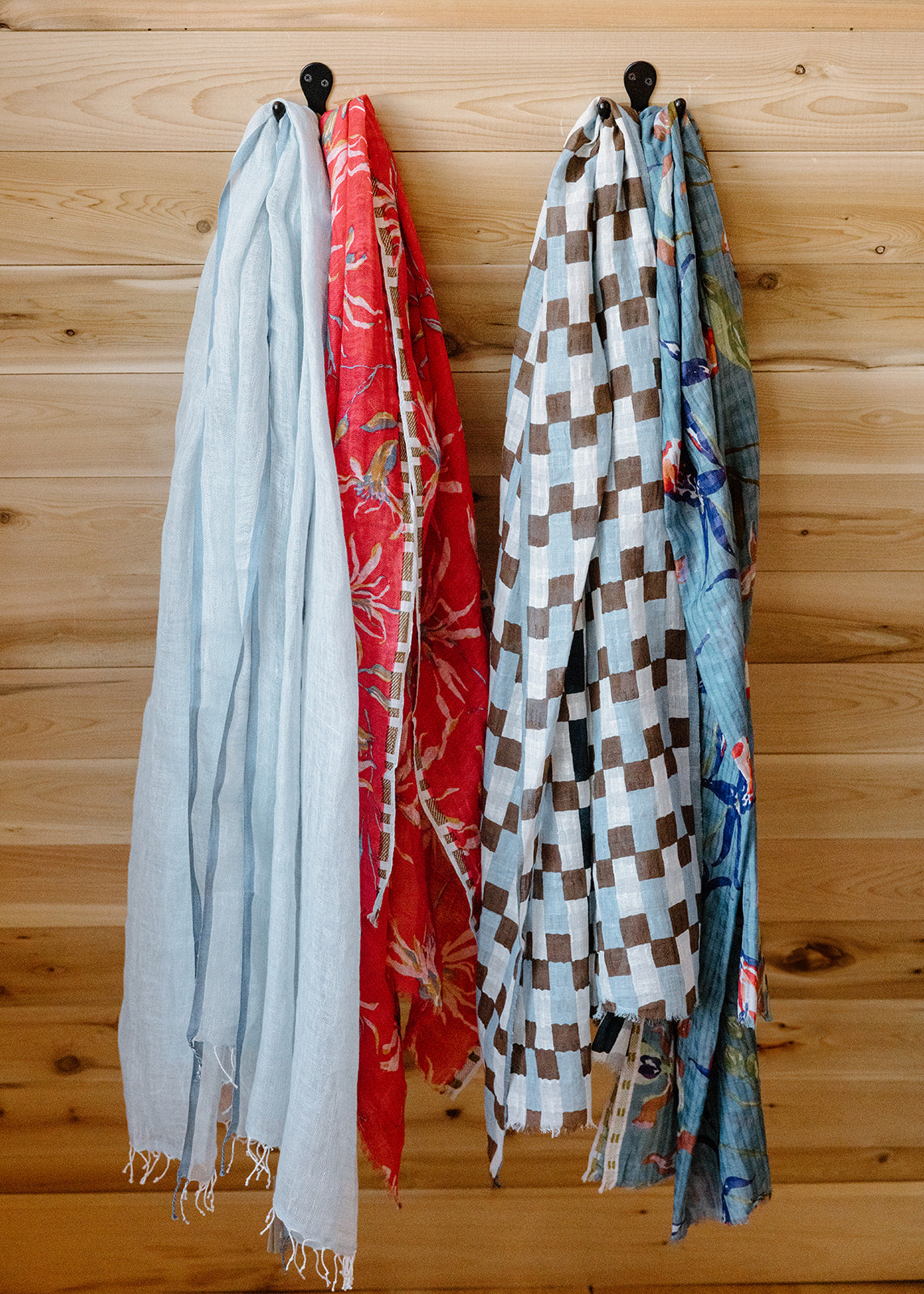 Four colorful scarves hanging on hooks against a wooden wall.