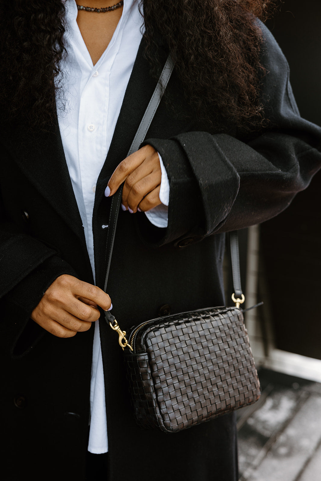 Woman in a black coat holding a woven shoulder bag.