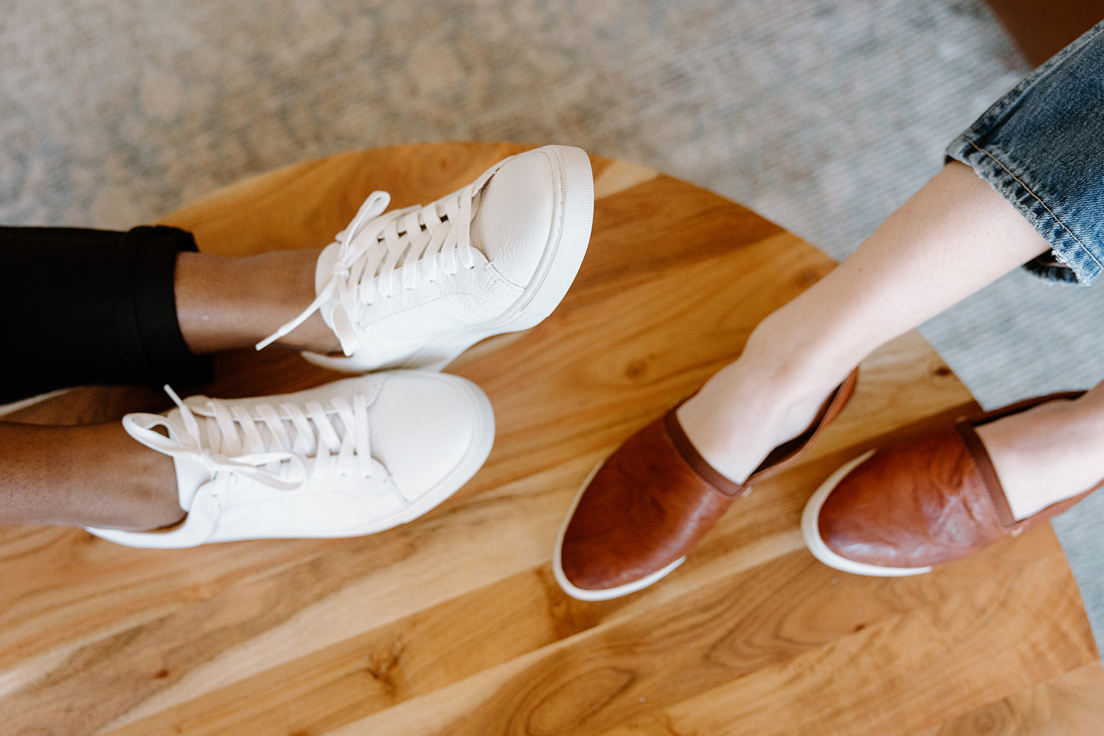 Two people sitting opposite each other, one wearing white sneakers and the other wearing brown leather shoes.