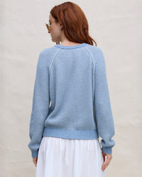A woman with long red hair, in sunglasses and the Margaret O’Leary Thermal Sweatshirt in Denim, stands facing away against a neutral background.