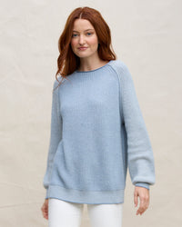 A woman with long red hair wears the Margaret O'Leary Baseball Tunic in Denim and white pants, standing against a plain, light background.