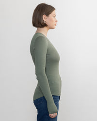 A woman with short brown hair, wearing the Margaret OLeary Shirtail Waffle Crew in Sage and blue jeans, stands in profile against a plain white background.