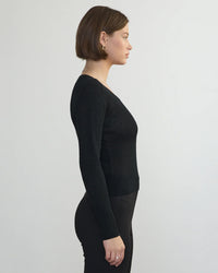 A woman with short brown hair stands in profile against a plain light background, wearing a black Margaret OLeary Scoop Neck Pullover and matching black pants.