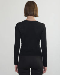 A person with short brown hair is seen from behind, wearing the Margaret OLeary Scoop Neck Pullover in Black and black pants, standing against a plain light background.