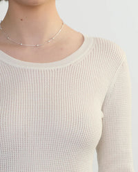 A person wears a delicate silver necklace and a cream-colored, textured waffle knit Margaret OLeary Scoop Neck Pullover in Ivory. The image is cropped to show the neck, shoulders, and upper chest.