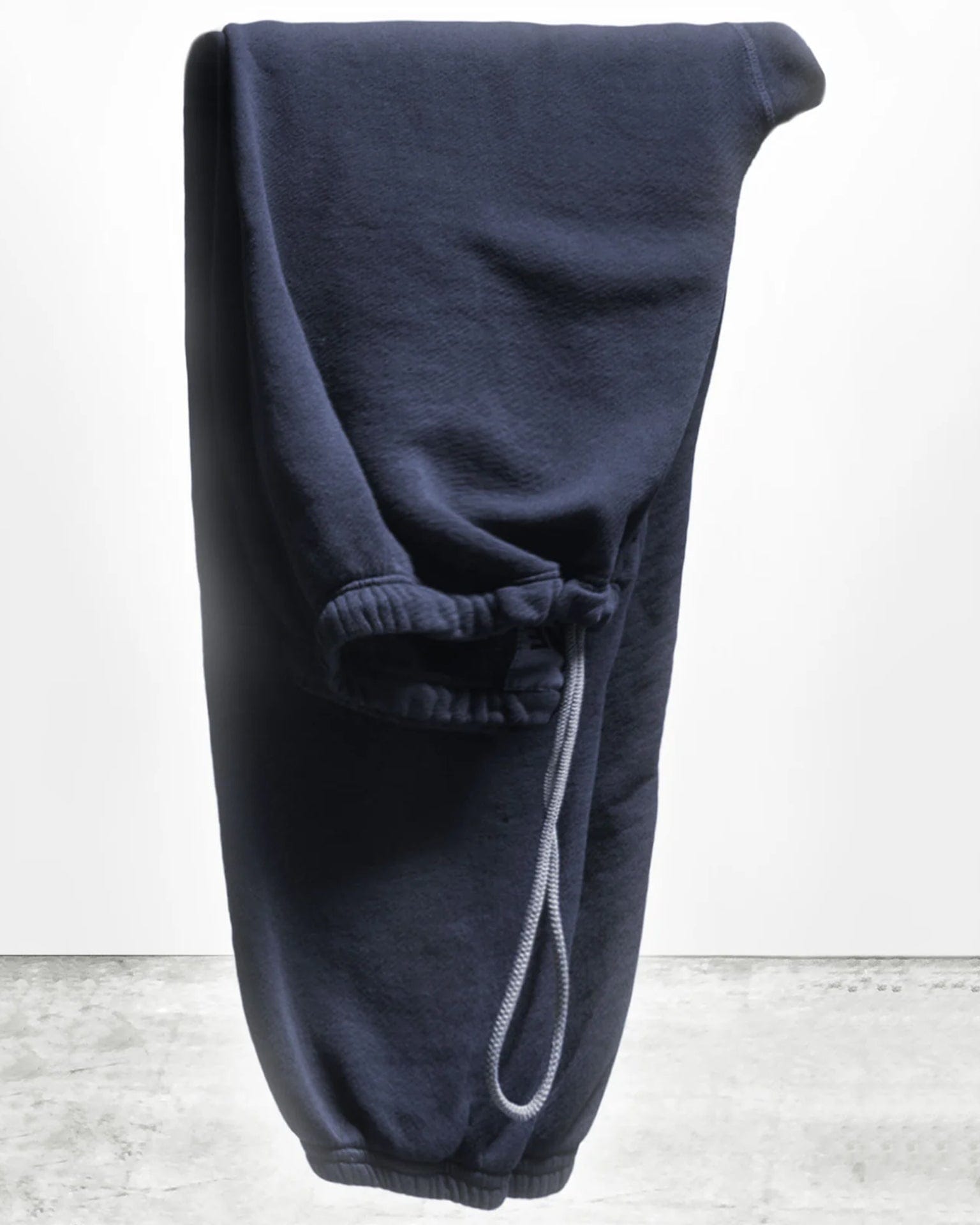 The Free City Basic Goodness OG Sweatpant in Moonshroom Blue is neatly folded and displayed upright, featuring an elastic waistband and drawstring, set against a plain white and gray background.