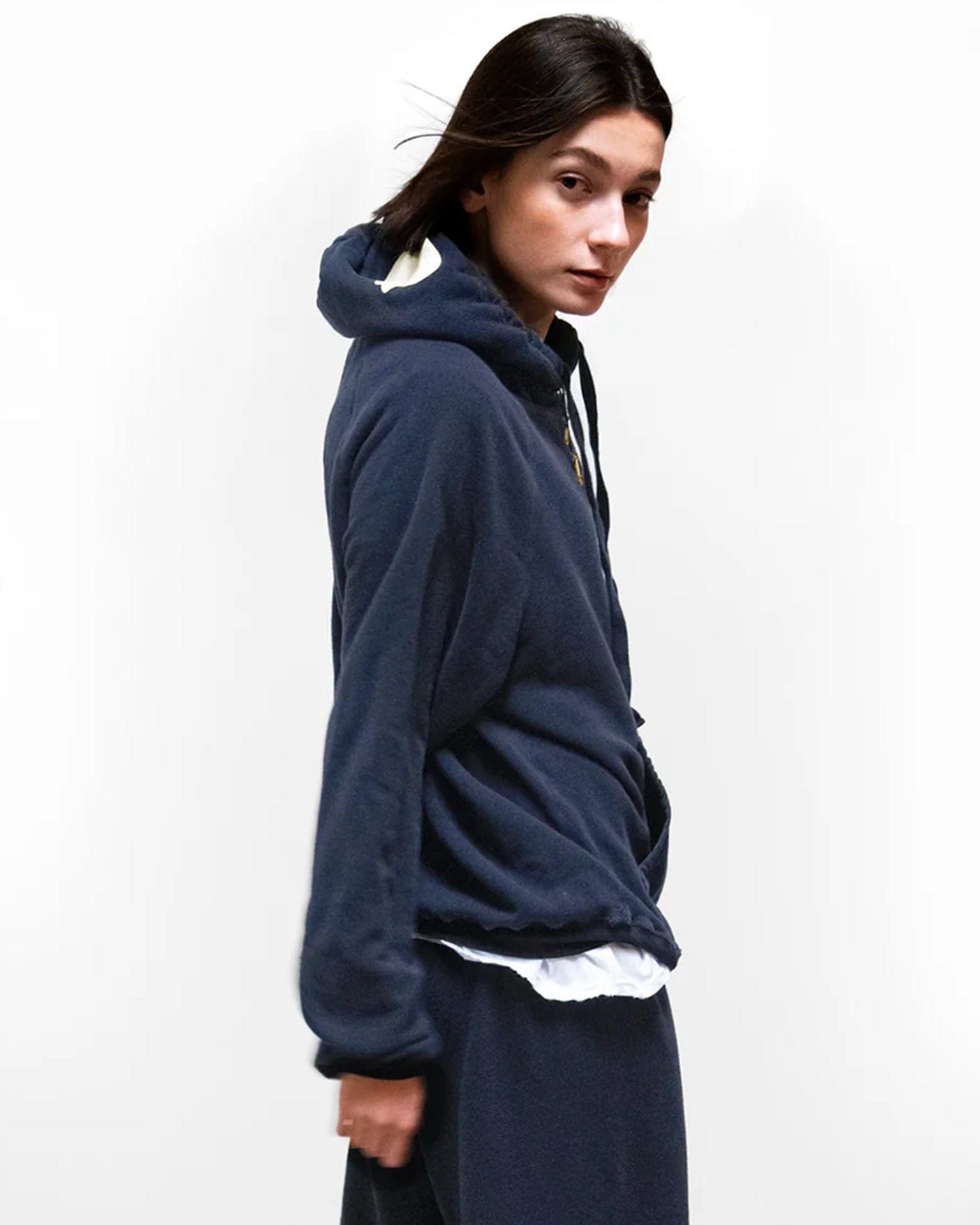 A person with straight dark hair wears the oversized Free City Basic Goodness Hoodie in Moonshroom Blue with matching pants over a white shirt, standing sideways and facing the camera against a plain white background.
