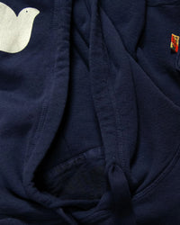 A close-up of the Free City Basic Goodness Hoodie in Moonshrooms shows a white bird graphic, colorful seam tag, and quality drawstring and stitching details on this light terry hoodie.