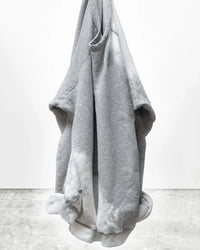 A Free City Rabbit Sweatshirt in Heather Bleachout hangs on a hook against a plain white wall and concrete floor, with the bottom corners slightly curled inward.