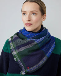 A woman wears a green and navy striped sweater and a Moismont Chai Wool Square Scarf No 752 in Royal Blue, looking slightly to the side against a plain background.