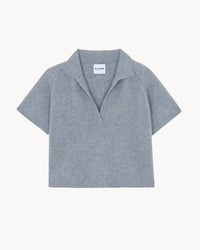 The Aenor Polo in Gris Chine by Kujten is a light gray, short-sleeved cashmere sweater featuring a wide collar, deep V-neck, and raglan sleeves, shown against a plain white background with the brand label on the neck tag.