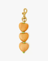 The Clare V. Heart Fob is a charming keychain featuring three wooden heart-shaped beads with green accents on a 14k gold-plated brass clasp—perfect for adding flair to your handbag.