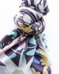 A close-up of the Épice Bold Daisy Wool Silk & Cashmere Scarf in Plum, showcasing its vibrant floral pattern in purple, green, blue, yellow, and pink.