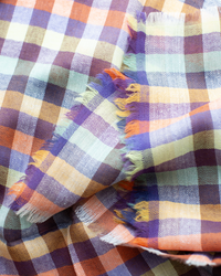 A close-up of the Épice Plaid Wool Bandana in Orange, showcasing its multicolored herringbone plaid pattern and frayed edges.