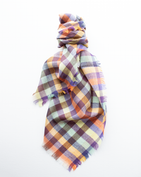 The Épice Plaid Wool Bandana in Orange, featuring frayed edges and purple, yellow, and blue tones, is displayed on a white background.