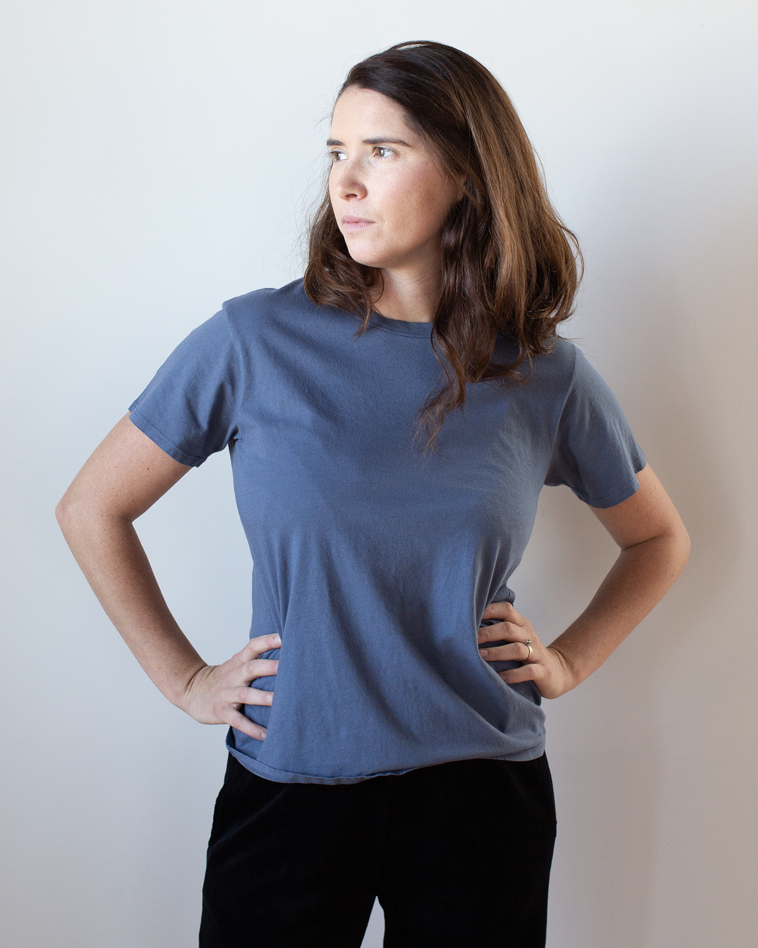 A woman with her hands on her hips wears the Moore Relaxed Fine Jersey Tee in Indigo by NSF, featuring a comfortable crew neck.