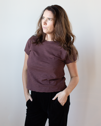 A woman with long brown hair wears the Velvet by Graham & Spencer Marie S/S Crop Top in Henna and dark pants, standing against a light background with her hands in her pockets, looking slightly to the side.