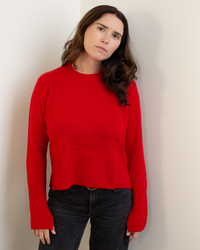 A woman with long, dark hair stands indoors against a white wall, wearing the Autumn Cashmere Cropped Boxy Crew W/ Slits in Blazer. She has a neutral expression and her arms rest by her sides.
