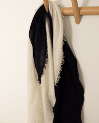 The Grisal Love Duo Mini in Navy X Milk, featuring fringed edges, hangs over a wooden hook mounted on a white wall.