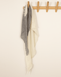 The Grisal Love Duo Mini in Milk X Heather Grey scarf hangs from a wooden wall hook rack against a plain light-colored wall.