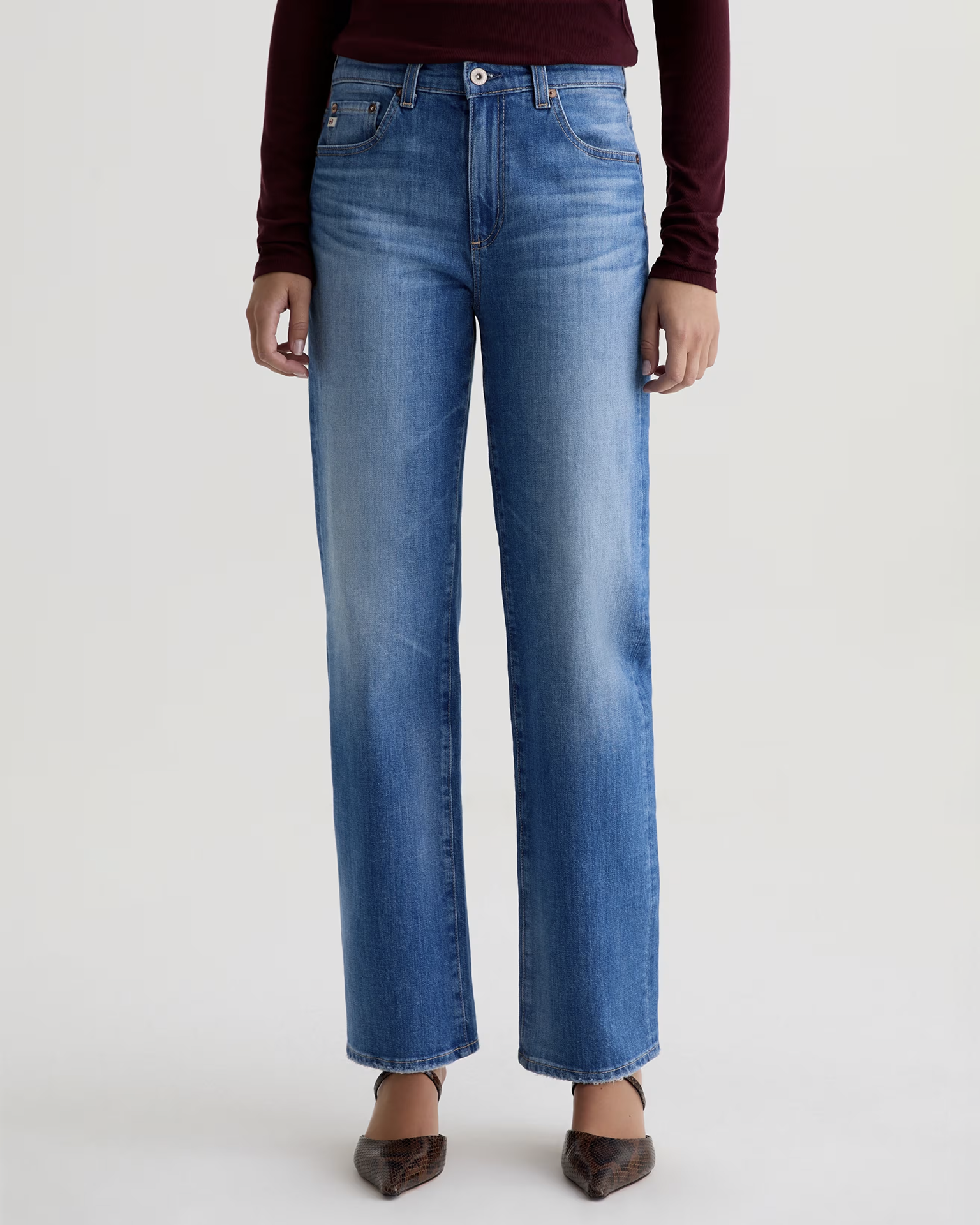 Model wearing The Brinley Straight in 13Ys Allure by AG Jeans, styled with a long-sleeve burgundy top and pointed brown shoes against a plain light background. Image is cropped at the shoulders.