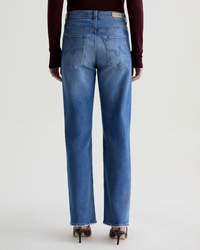 A person is shown from the back wearing AG Jeans' The Brinley Straight in 13Ys Allure, styled with a maroon long-sleeve top and heeled sandals against a plain light background.